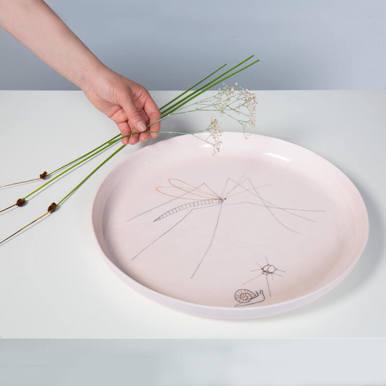 Deze grote platte schaal in de kleur nude is een ontwerp van Harm & Elke. Ze maakten 'm van porselein en illustreerden het bord met fragiele insecten.