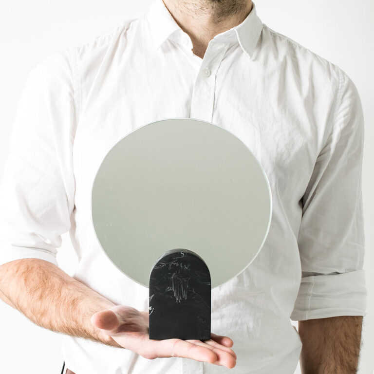Nathan van House Raccoon uit België houdt hier Archie Mirror in zijn hand. De design spiegel staat op een zwarte stevige voet die lijkt op zwart marmer.