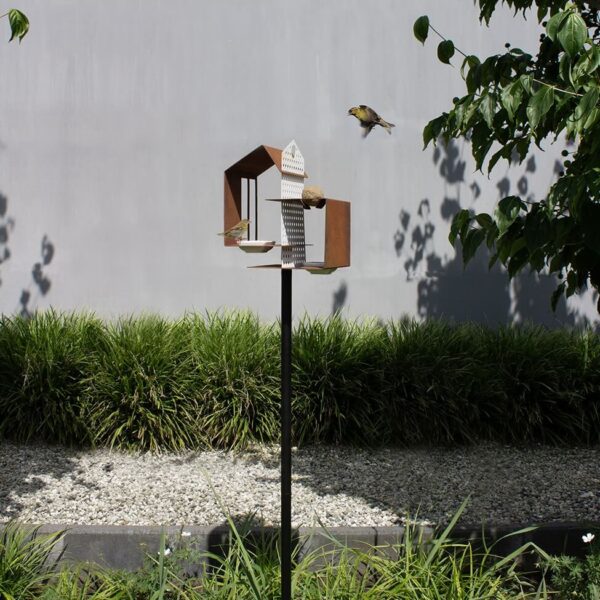 Het Tweet house cortenstaal vogelvoederhuis staat op een hoge zwarte paal.