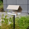 Open Diamond modern vogelvoederhuisje in zandkleur op hoge grijze paal in moderne tuin