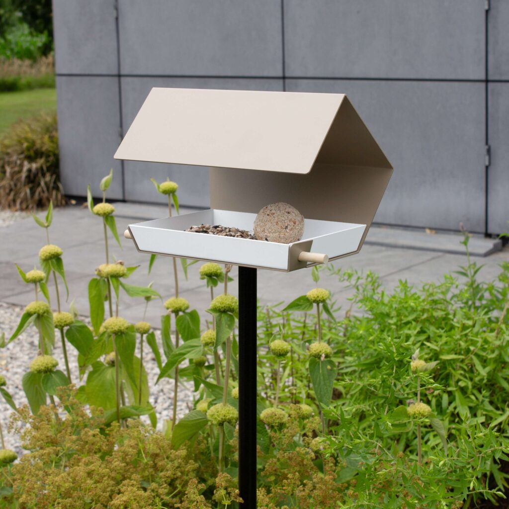 Open Diamond modern vogelvoederhuisje in zandkleur op hoge grijze paal in moderne tuin